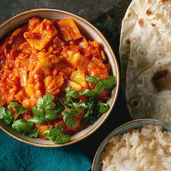A bowl of vegetable curry with a side of basmati rice and naan bread. 
