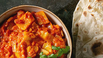 A bowl of vegetable curry with a side of basmati rice and naan bread. 